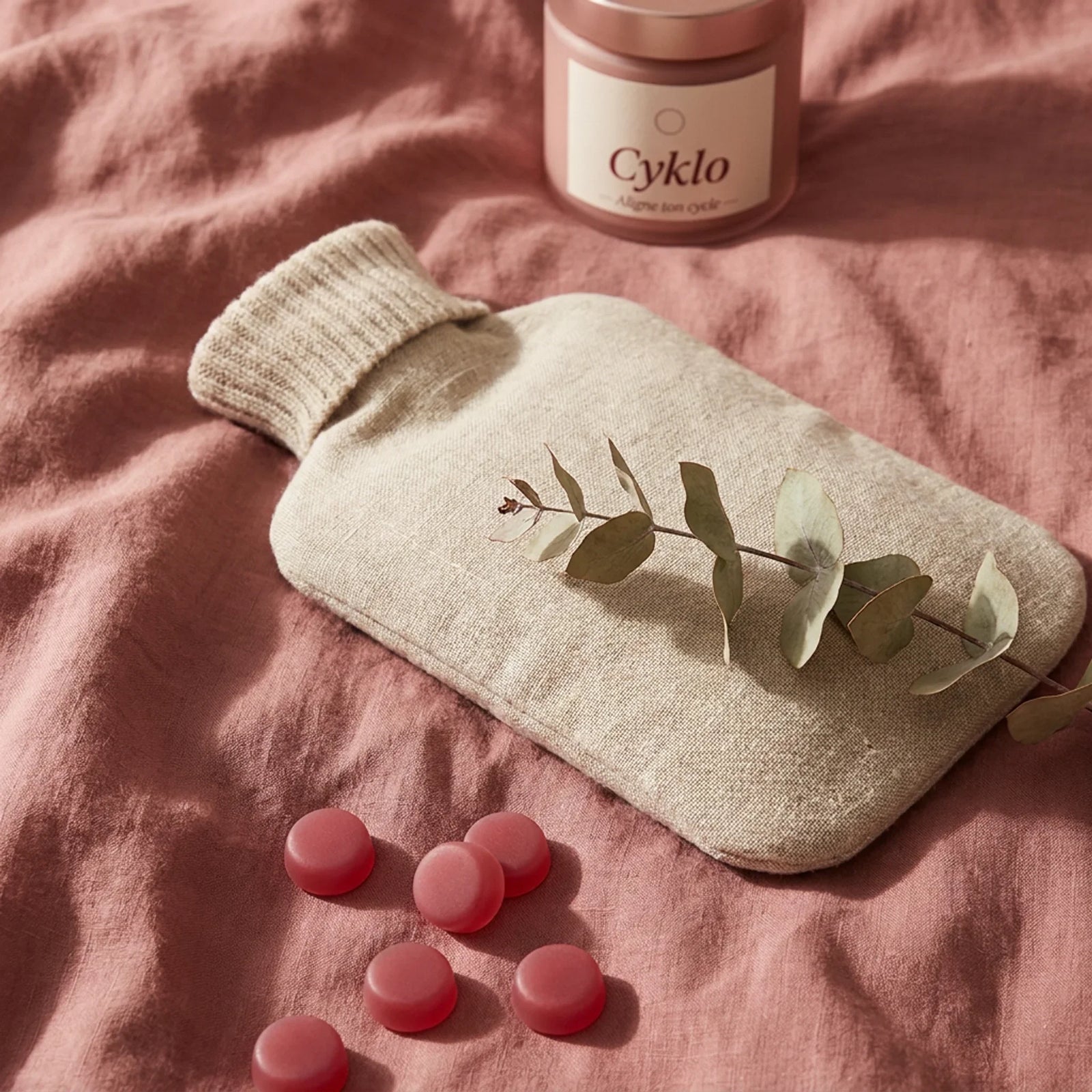 Bouillotte et gummies Cyklo Days sur lit rose nude, solution naturelle contre le mal de ventre pendant les règles